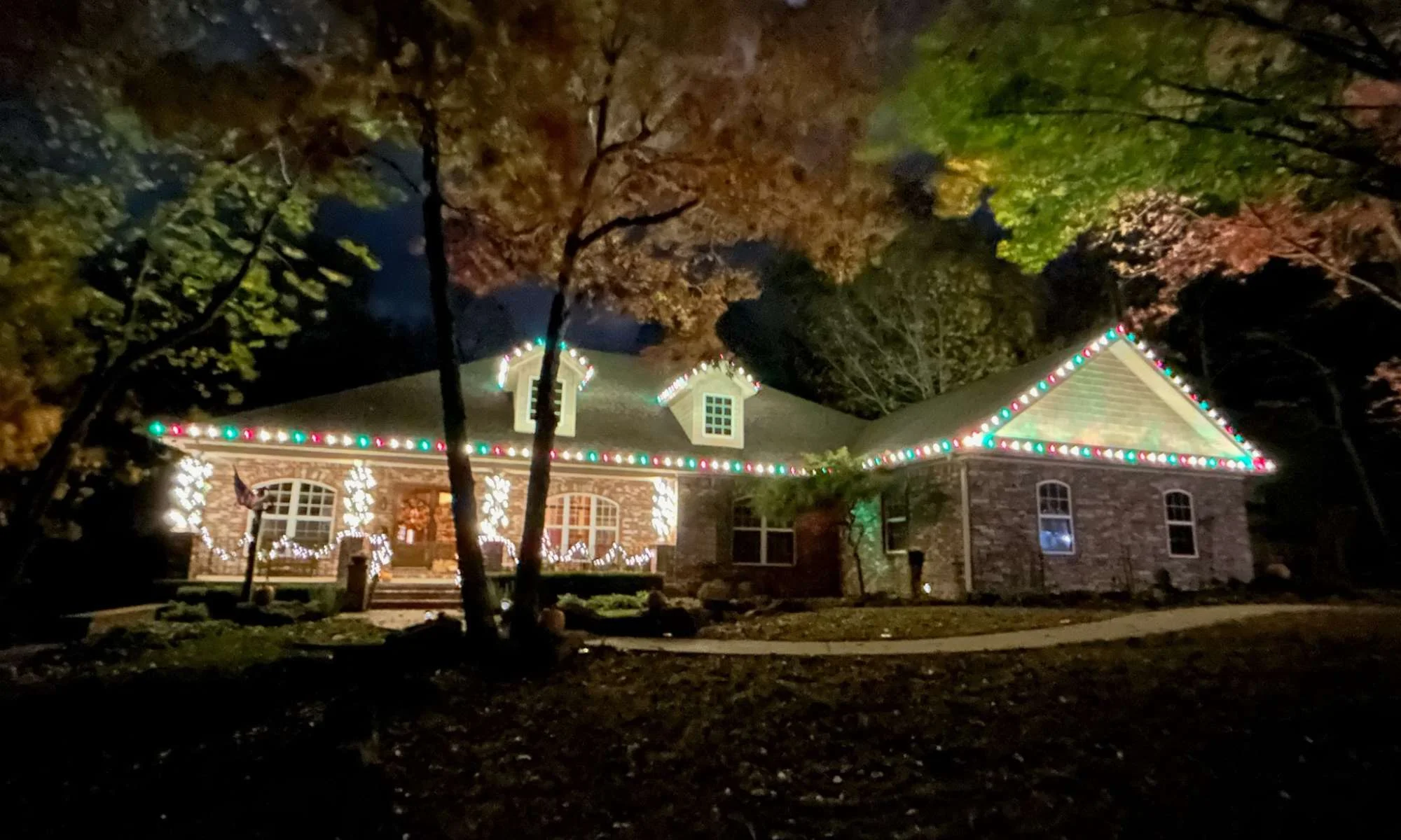 Single-story home with multicolor Christmas lights installed on the roofline at night